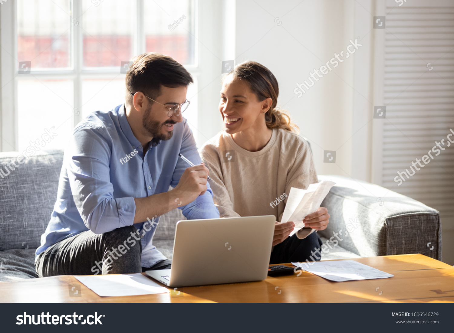 Happy young married couple sit on couch calculate expenses use easy online banking service at home, smiling millennial husband and wife count taxes house expenditures pay bills on internet #1606546729