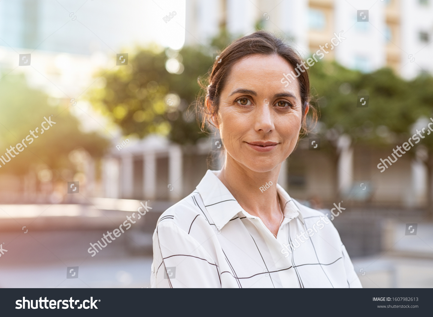 Portrait of happy mature businesswoman looking at camera. Successful proud woman in city street at sunset. Satisfied latin business woman in formal clothing smiling outdoors. #1607982613