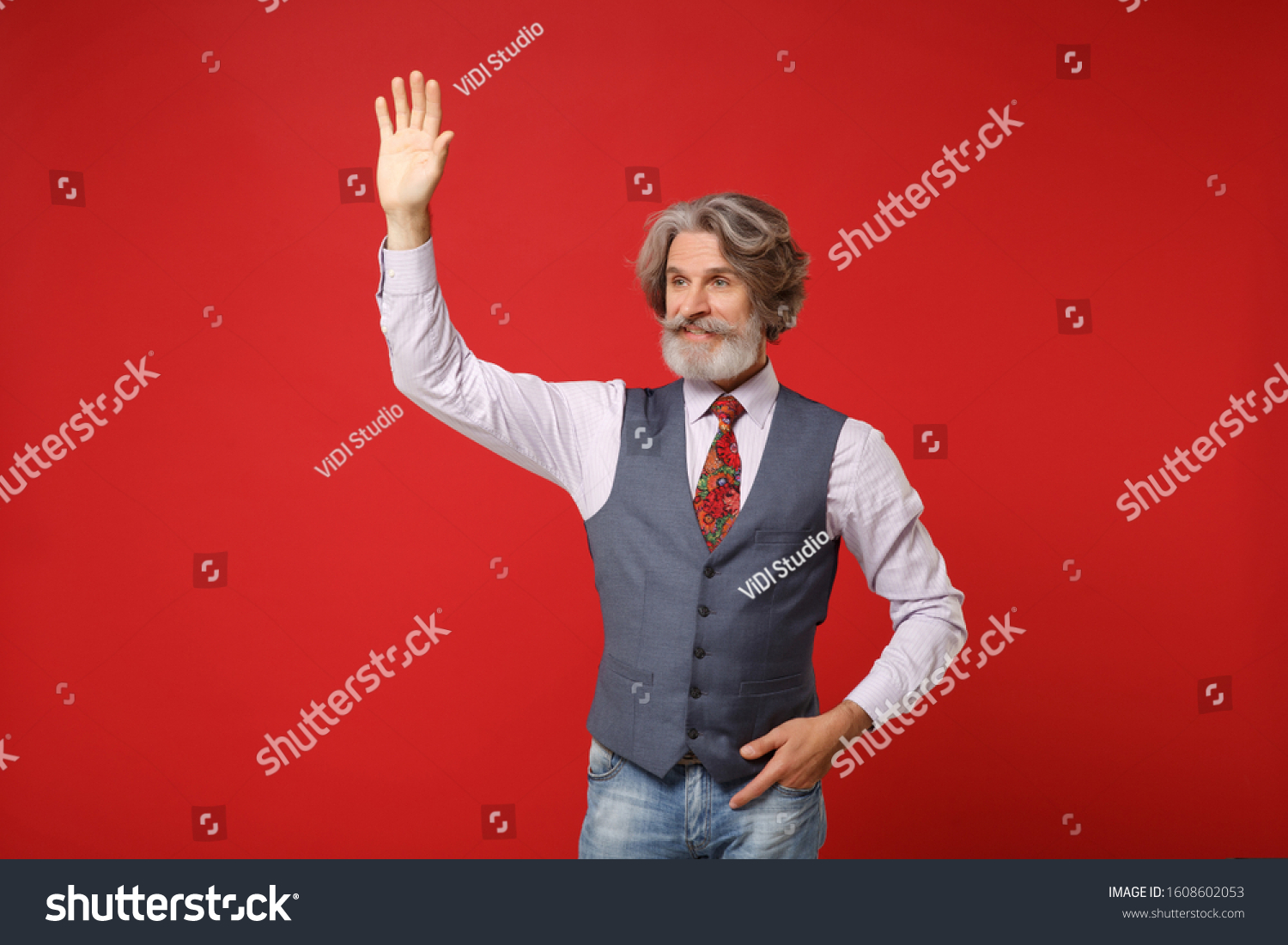 Elderly gray-haired mustache bearded man in classic shirt vest colorful tie isolated on red background. People lifestyle concept. Mock up copy space. Waving and greeting with hand as notices someone #1608602053