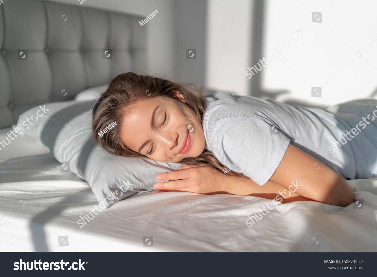 Bed Asian girl happy smiling sleeping on stomach sleeper resting head on foam pillow. Healthy sleep. #1608735547