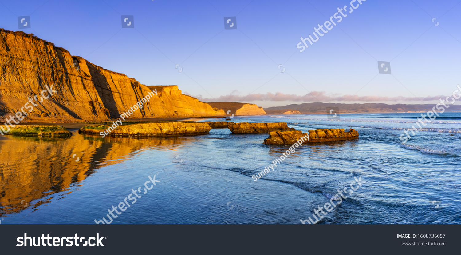 Sunset view of the Pacific Ocean shoreline, with golden colored cliffs reflected on the wet sand, Drakes Beach, Point Reyes National Seashore, California #1608736057