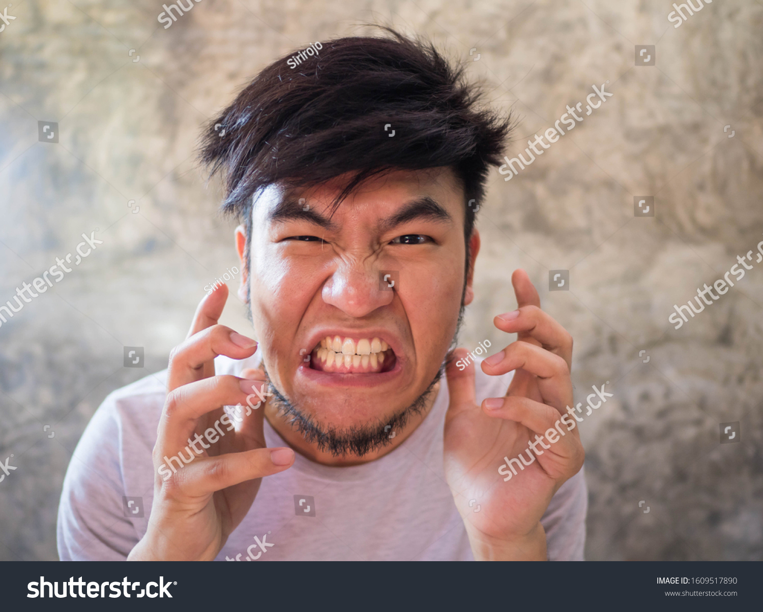 Asian man with a beard wearing a white T-shirt Expressing anger, resentment, anger, and anger, and able to destroy everything that is close to him In a cement backdrop There is space for copy space. #1609517890