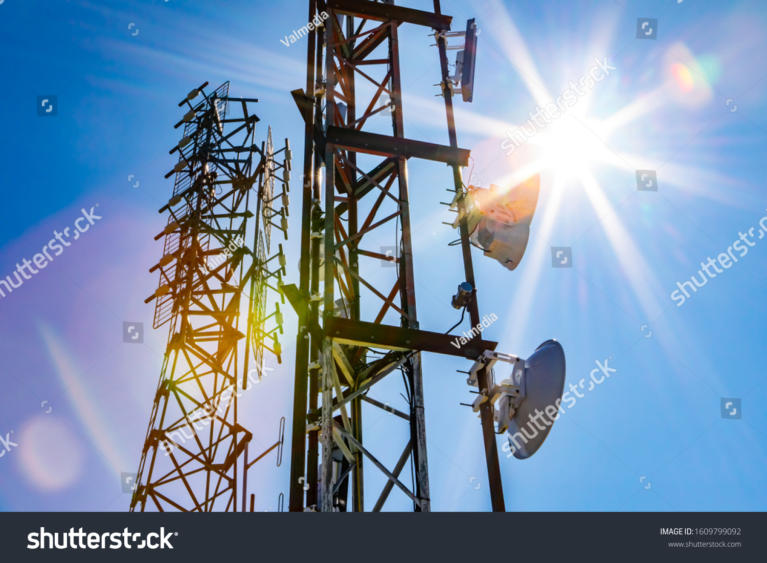 Bright sun shine over two cell site towers, radio and GPS transmitter and receiver, associated with electromagnetic pollution, with vibrant lens flare #1609799092