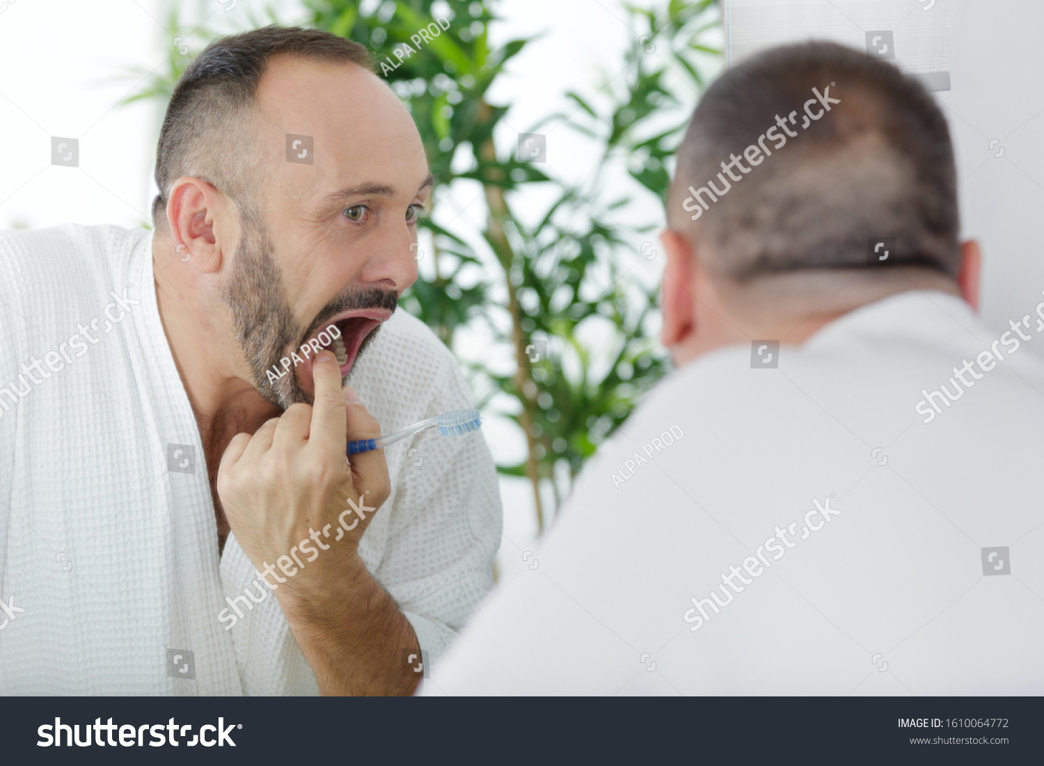 mature man checking his teeth in the mirror #1610064772