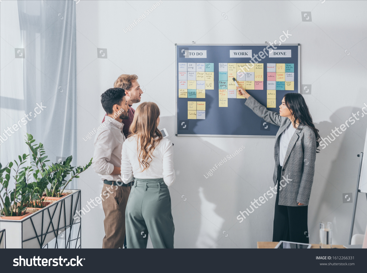 attractive asian scrum master pointing at db design letters on sticky note near businessmen and businesswoman #1612266331