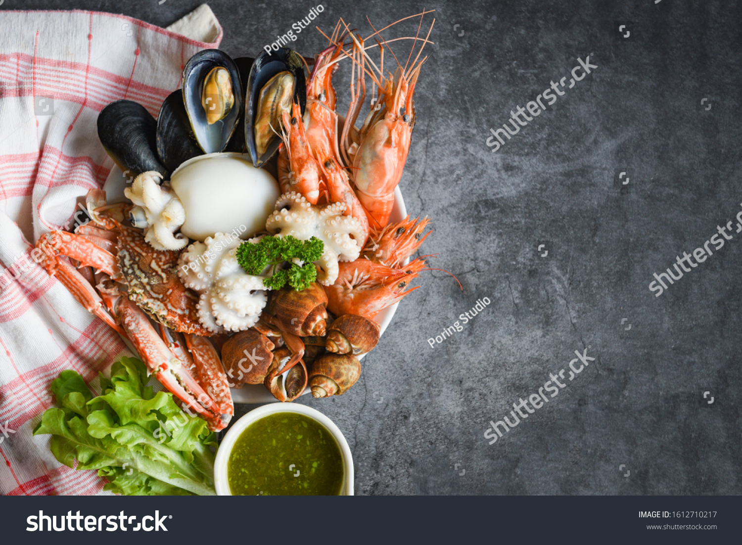 Fresh shrimps prawns squid mussels  spotted babylon shellfish crab and seafood sauce lemon on plate black stone background top view copy space / Cooked steamer food served seafood buffet concept  #1612710217