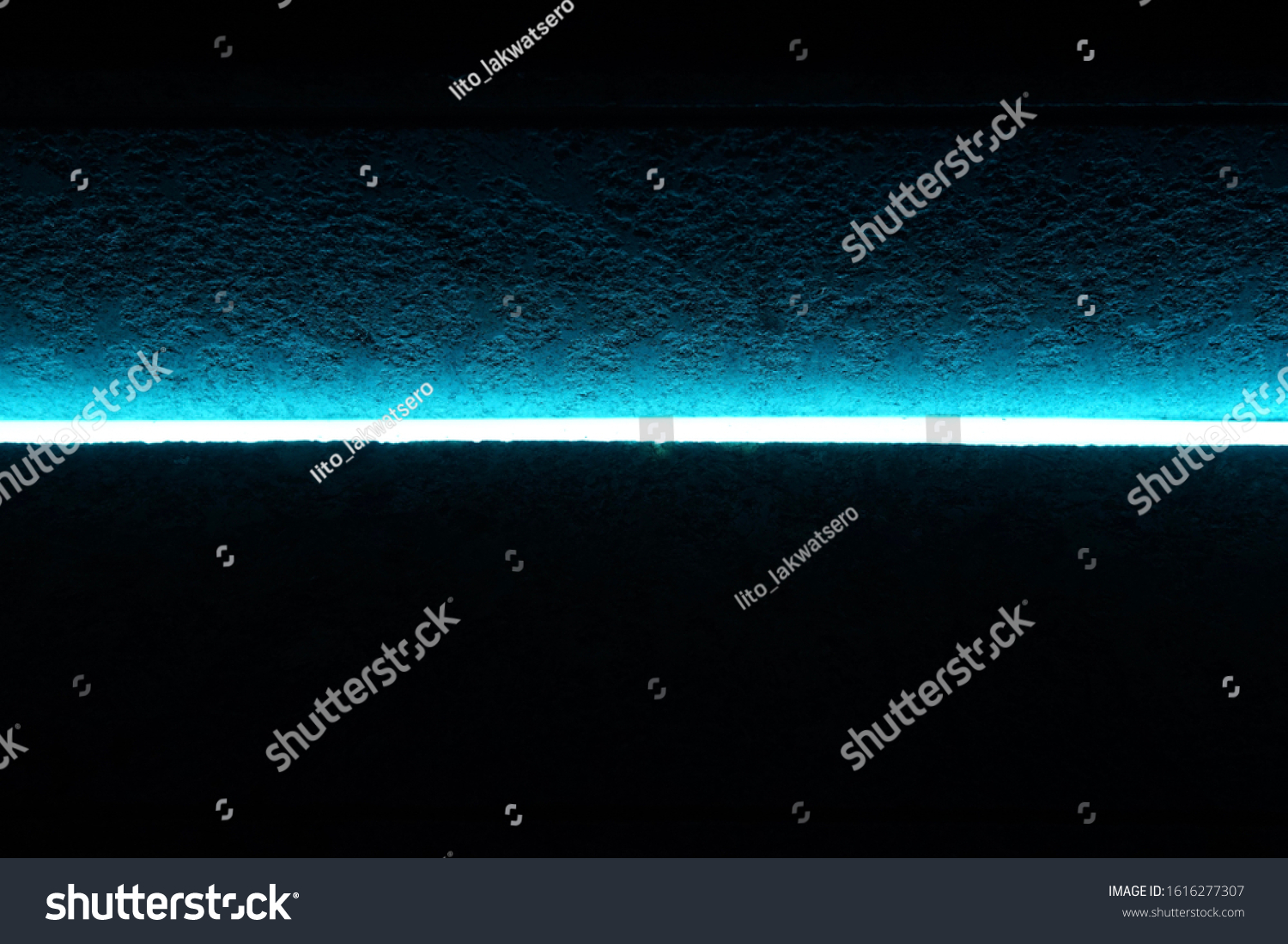 A narrow blue neon light glows in the dark to partly illuminate a rough cement surface #1616277307