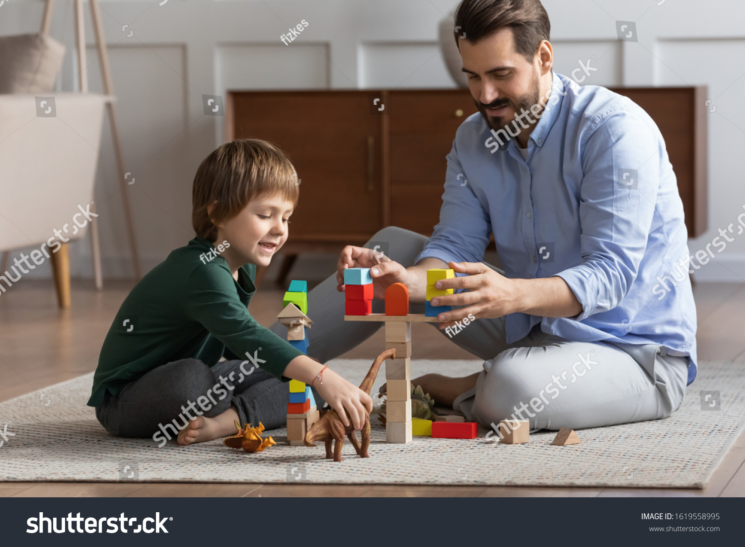 Loving young father sit on floor with cute little son engaged in funny childish activity in living room together, caring dad have fun play with small boy child involved in interesting game at home #1619558995