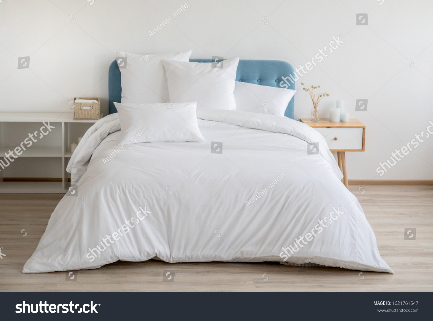 Interior with white bed linen on the sofa. Bedroom with bed, white bedding, and bedside table. White pillows, duvet and duvet case on bed with blue headboard. Front view. #1621761547