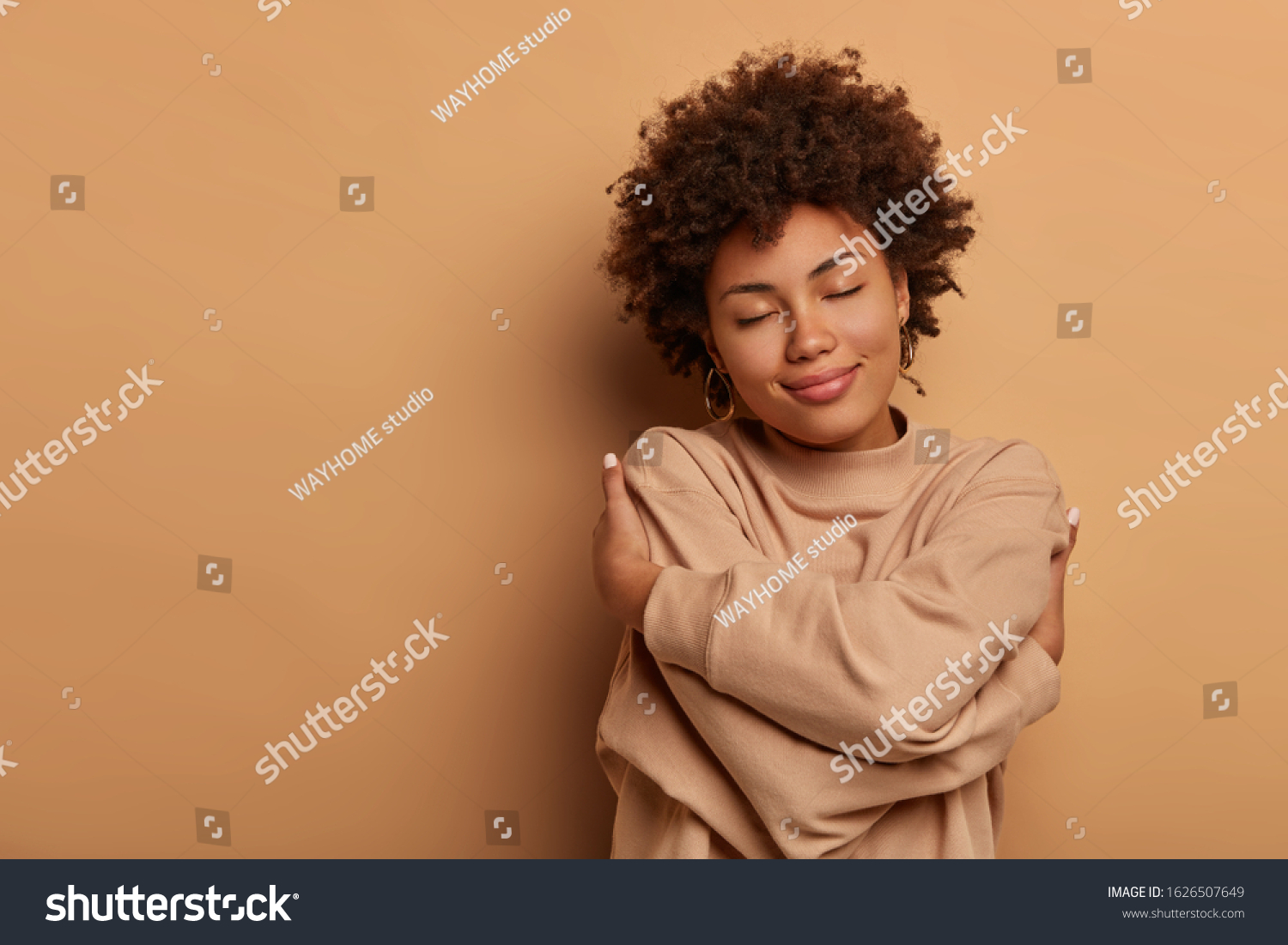 Love yourself, self acceptance. Gentle lovely Afro American woman crosses hands and embraces own body, tilts head and closes eyes, wears comforable brown sweater, models indoor. I love myself #1626507649