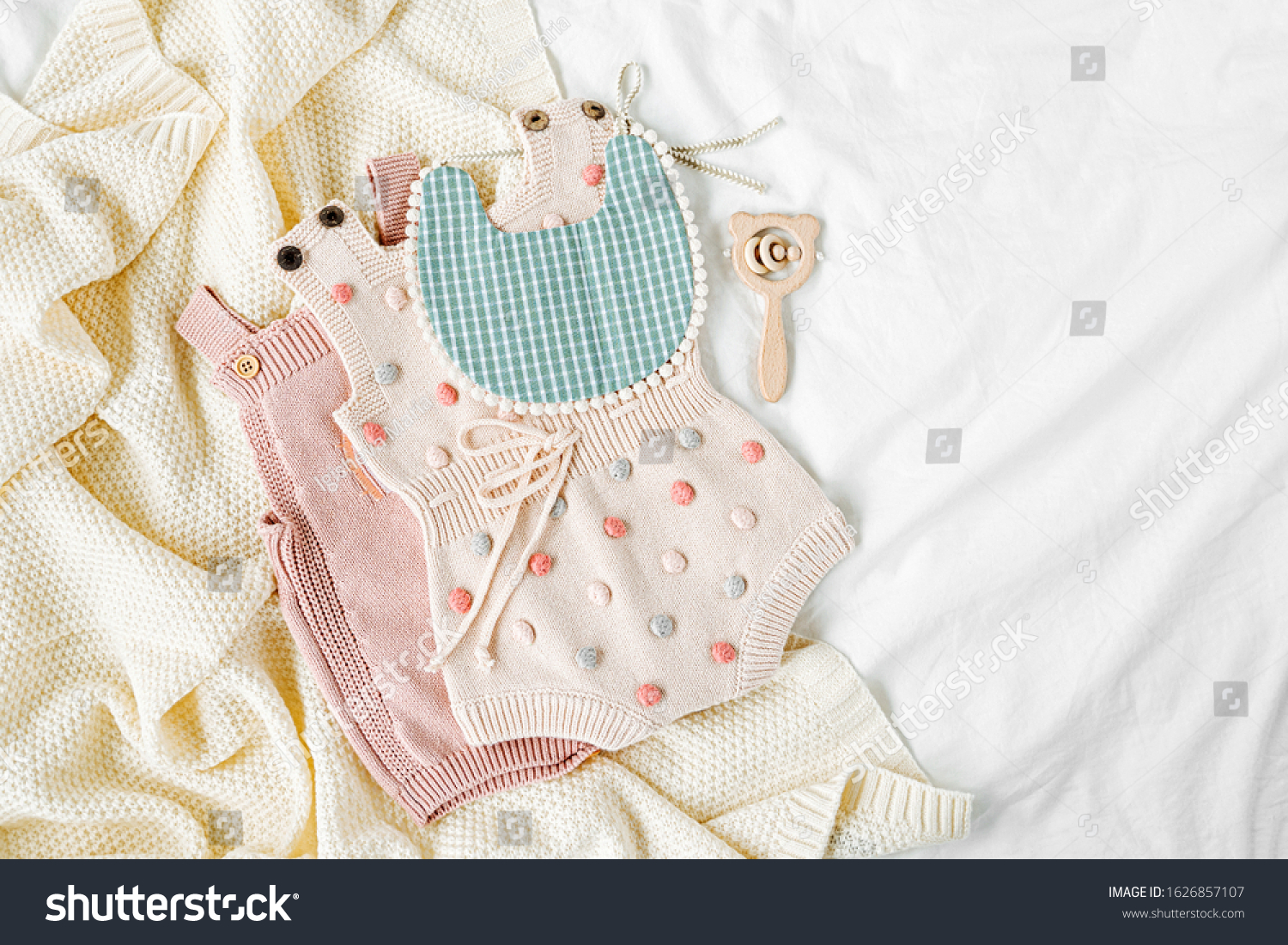Pink bodysuit and  bib on knitted blanket. Set of  kids clothes and accessories  on bed. Fashion newborn. Flat lay, top view #1626857107