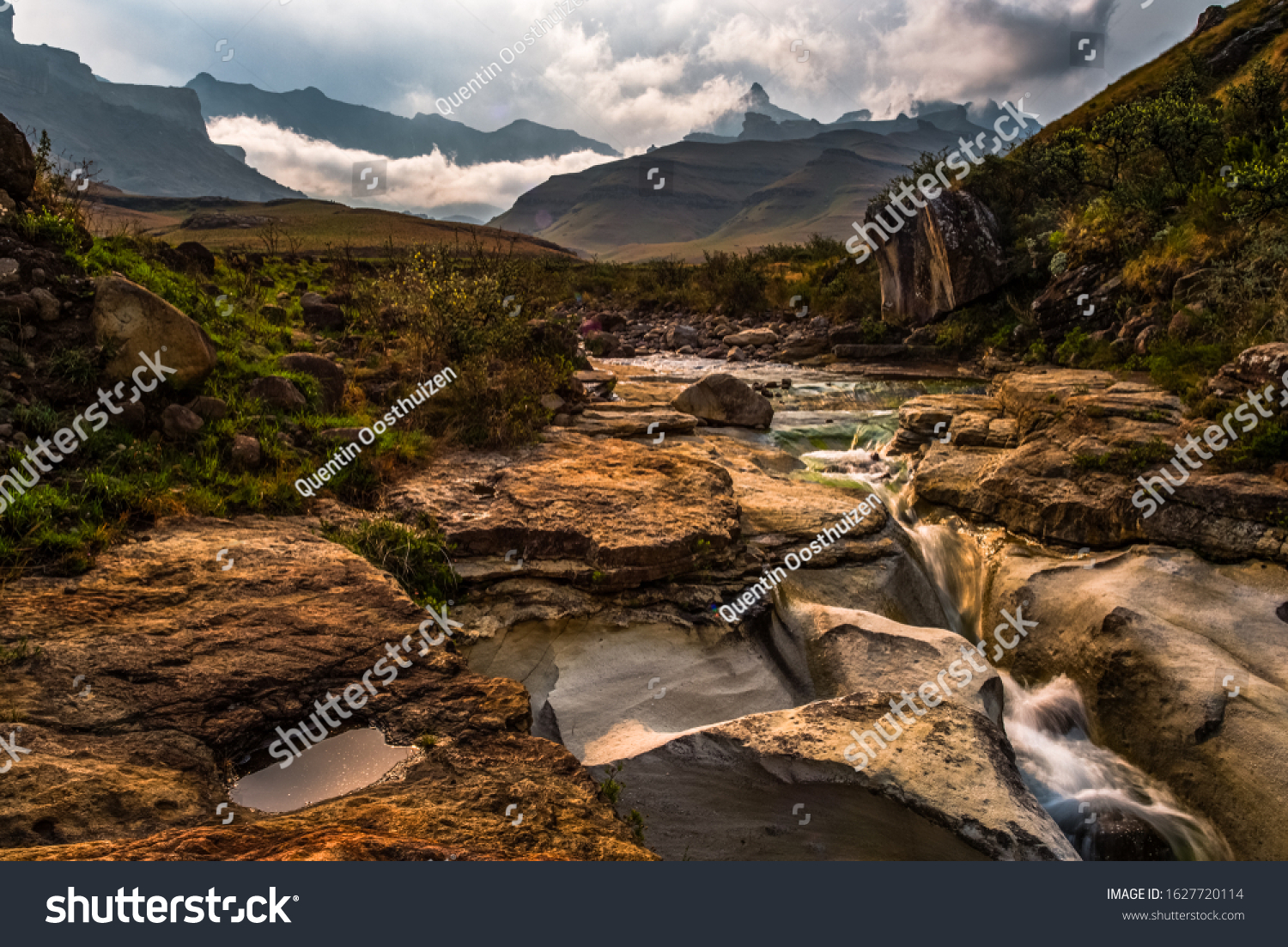 Stream filtering through the rocks with clouds over Rhino Peak in  Garden Castle Drakensberg South Africa #1627720114