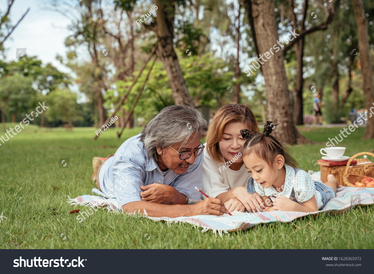 Grandmother,Grandfather and grand daughter enjoying sunny garden holiday together, outdoors space, leisure lifestyle,happy teaching with flare light sky in park. #1628365972