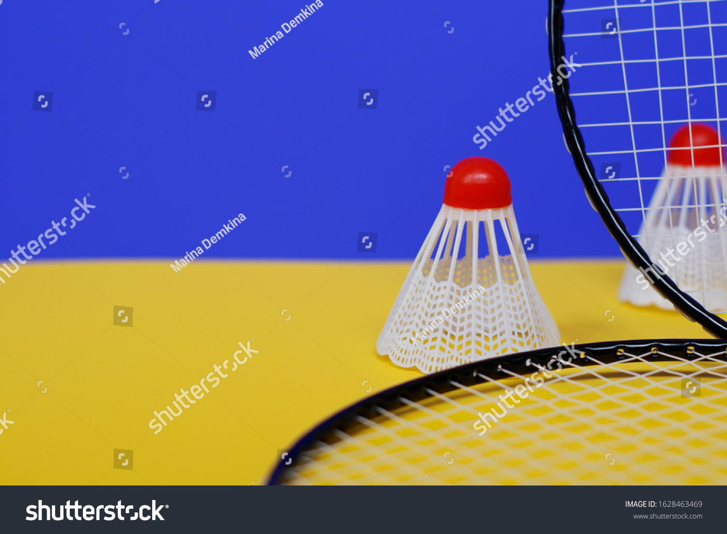 Badminton. Two shuttlecocks and two badminton racket. The colored background is blue and yellow. Idea for a magazine. #1628463469