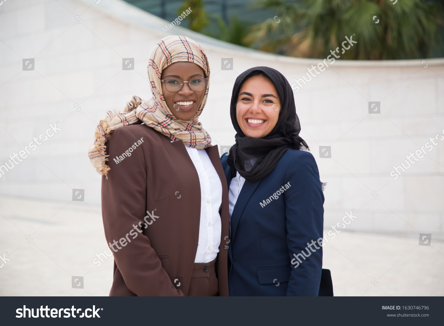 Two confident Muslim women looking at camera. Beautiful cheerful businesswomen posing on street. Female confidence concept #1630746796