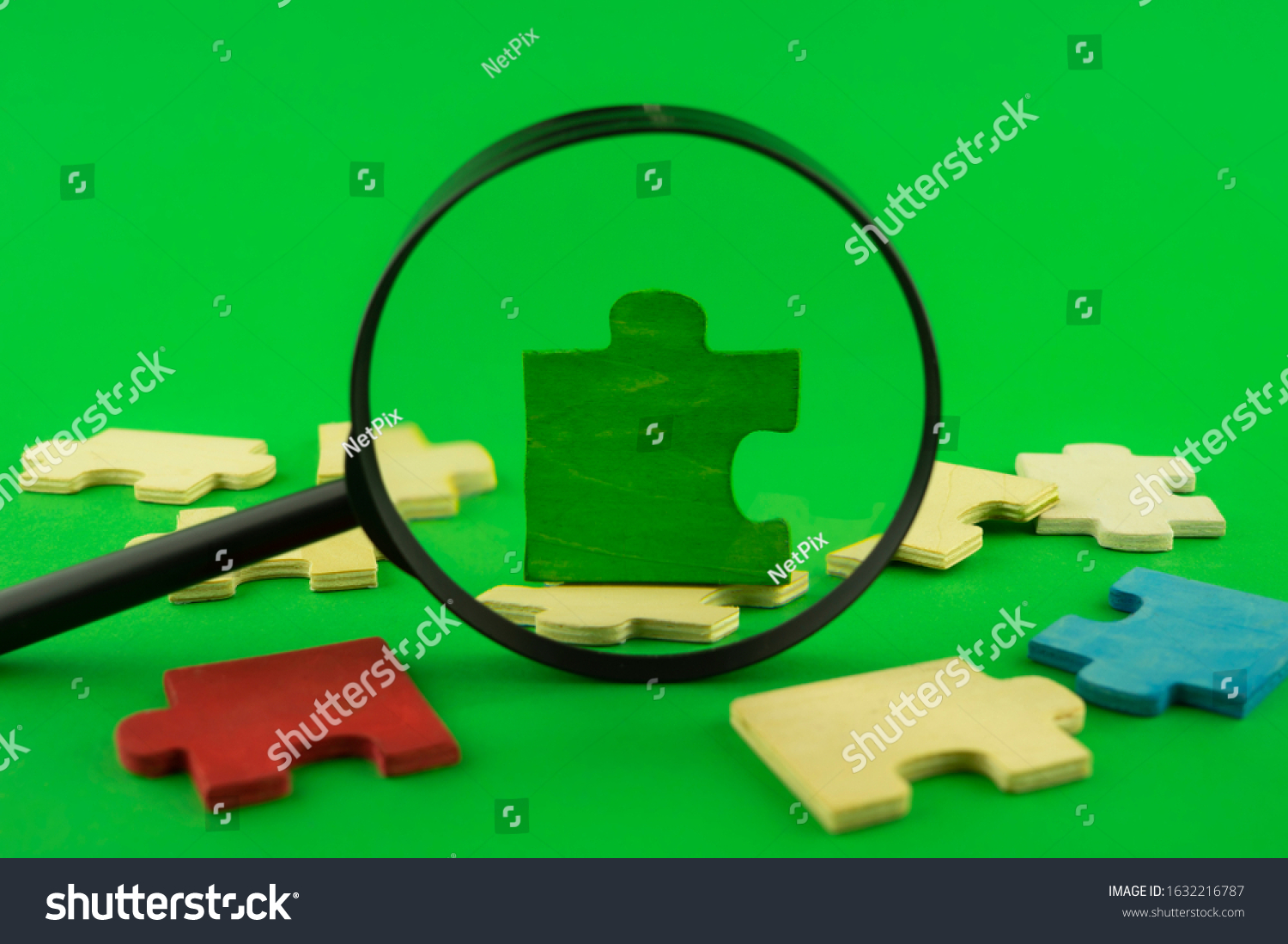 Colorful jigsaw puzzle pieces with magnifying glass focused on a single green corner piece in a conceptual image over green for search, investigation and problem solving #1632216787
