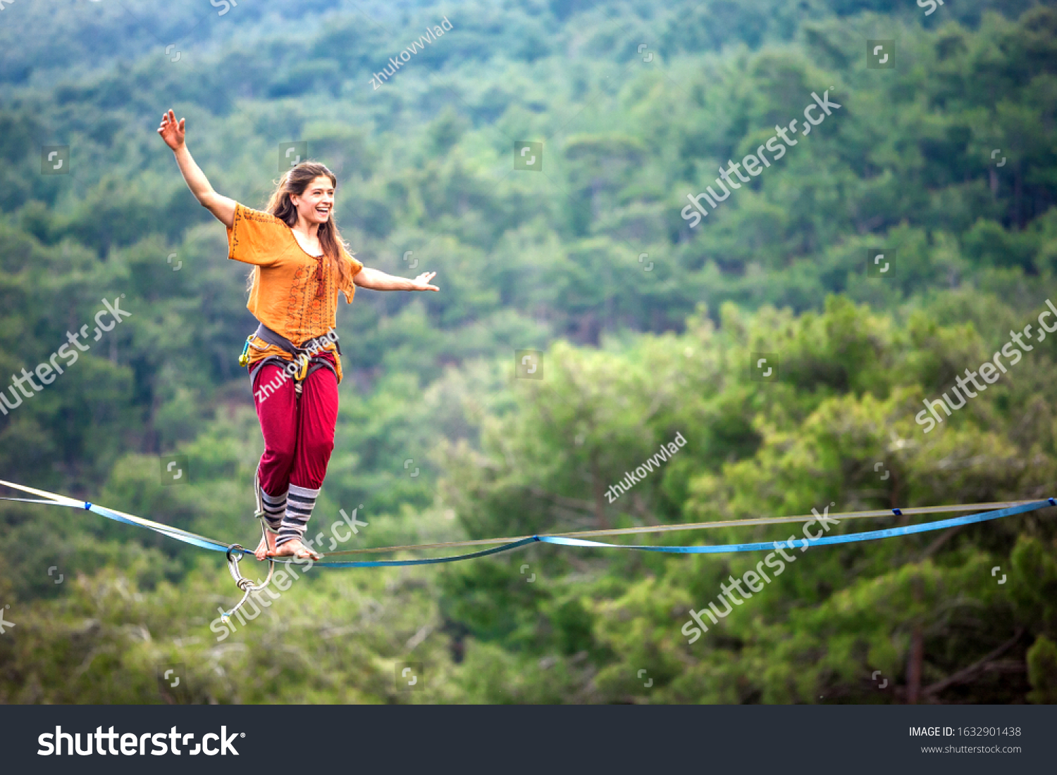 Highliner on a rope. Highline on a background of mountains. Extreme sport on the nature. Balancing on the sling. Equilibrium at altitude. A woman catches balance on the line.  #1632901438