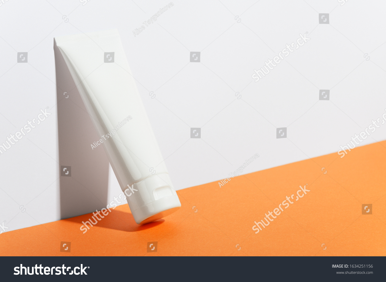 Cream tube on bright sunny orange background. Cosmetic skincare product blank plastic package. White unbranded lotion, balsam, hand creme, toothpaste mockup. Sunscreen cream bottle #1634251156