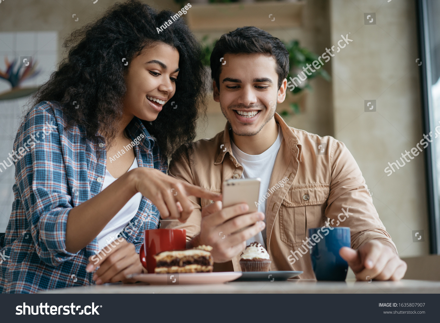 Happy couple using mobile phone application for online shopping. Emotional friends communication, laughing, looking at digital screen, sitting together in cafe  #1635807907