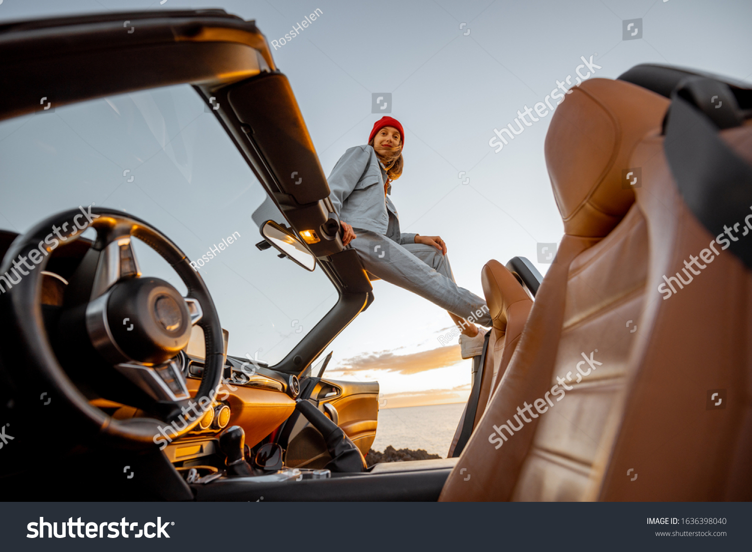 Woman enjoying beautiful view on the ocean, sitting on the car roof top during a sunset. Nature enjoyment and carefree travel by car concept #1636398040