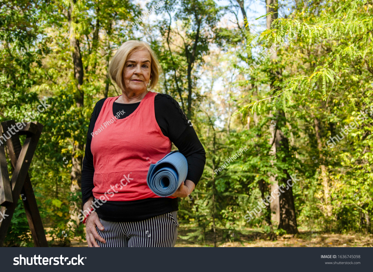 Old senior woman with yoga mat outdoors in green woods going on training.Healthy lifestyle and exercise in retirement.Grey hair matured  female workout outdoors.Copy space #1636745098