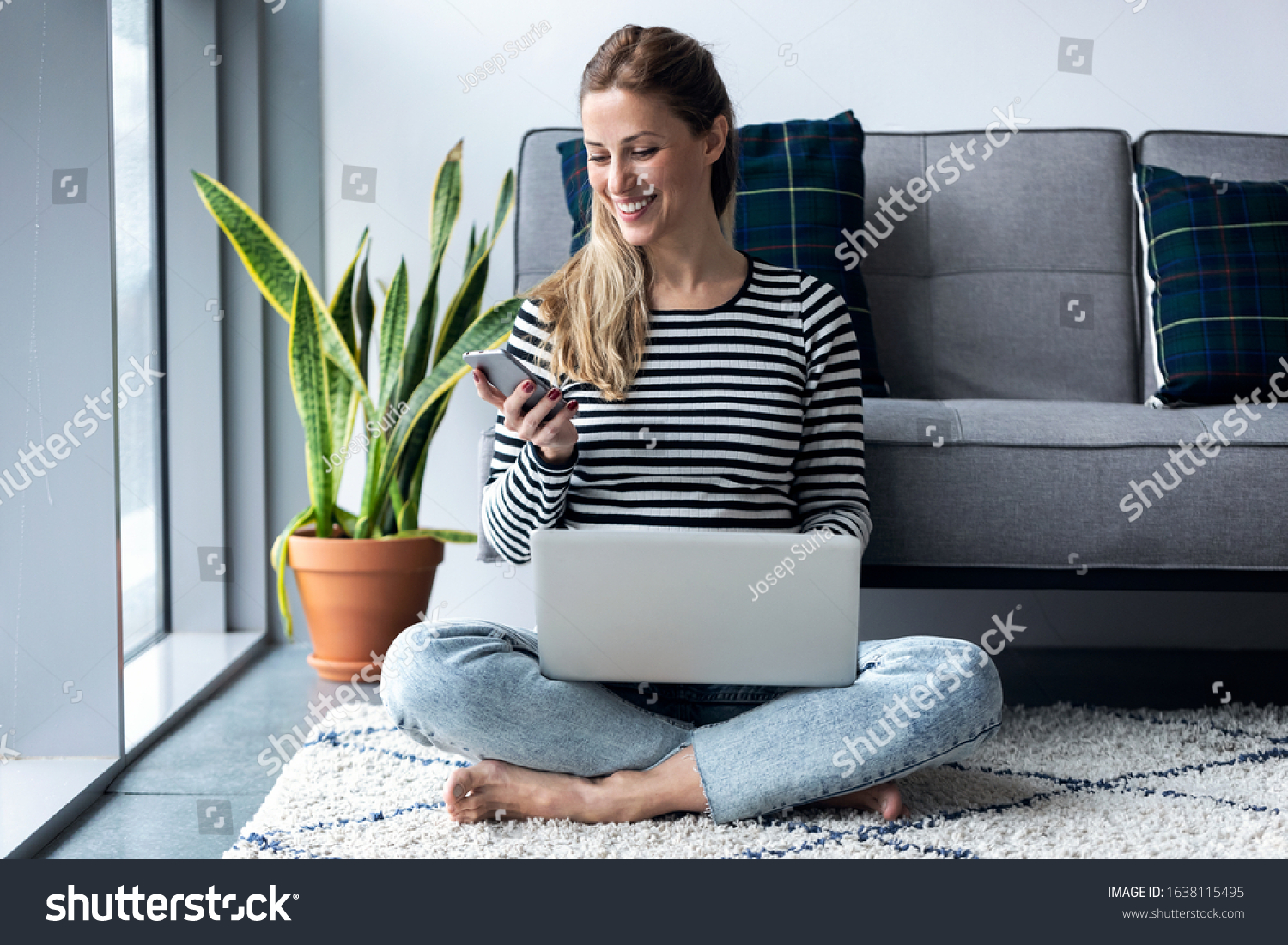Shot of pretty young woman using her mobile phone while working with laptop sitting on the floor at home. #1638115495