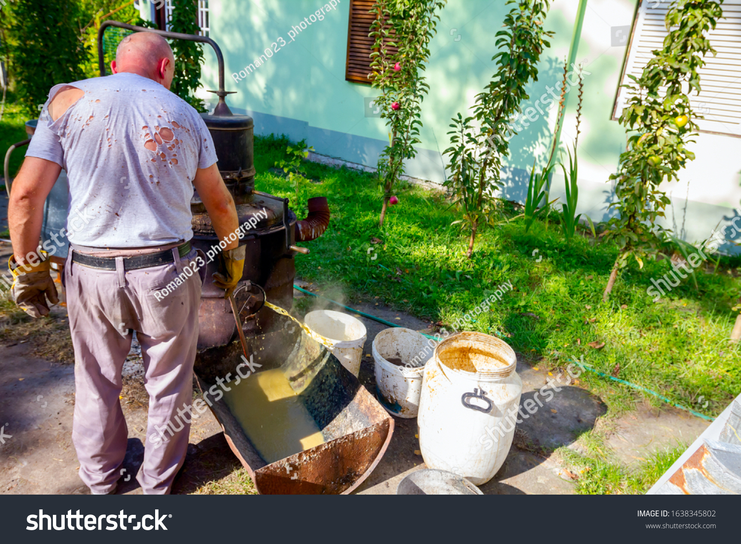 Man is unloading boiler of homemade distillery made of copper to release used fruit marc, making moonshine schnapps, alcoholic beverages such as brandy, cognac, whiskey, bourbon, gin, and scotch. #1638345802