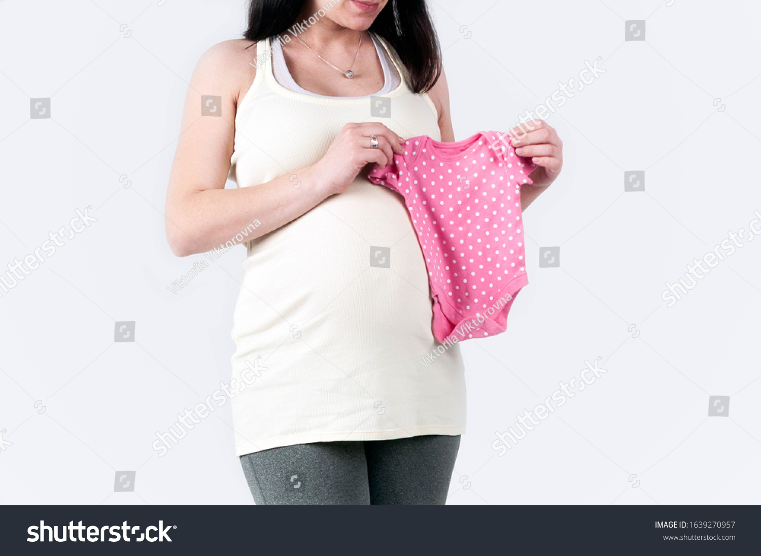 cropped view of pregnant woman in beige blouse holding near belly pink dotted bodysuit for newborn isolated on white, baby expectation concept #1639270957