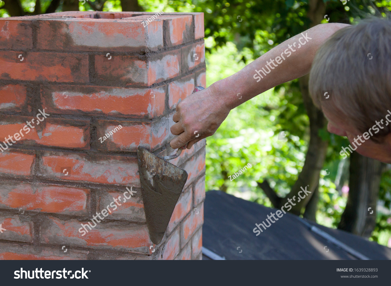 A man making masonry works, working with a trowel and making a chimney of red bricks #1639328893