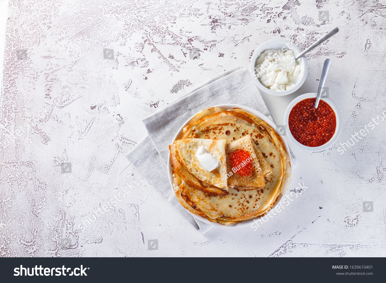 Traditional Russian Crepes Blini stacked in a plate with red caviar, fresh sour cream on light background. Maslenitsa Russian festival meal. Russian food, russian kitchen. Top view. Space for text #1639610401
