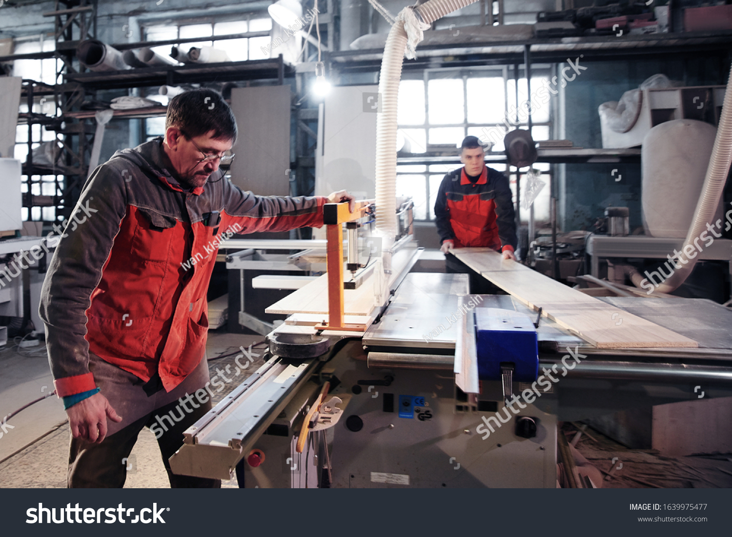 Process of production and manufacture of wooden furniture in furniture factory. Worker carpenter man in overalls processes wood on special equipment #1639975477