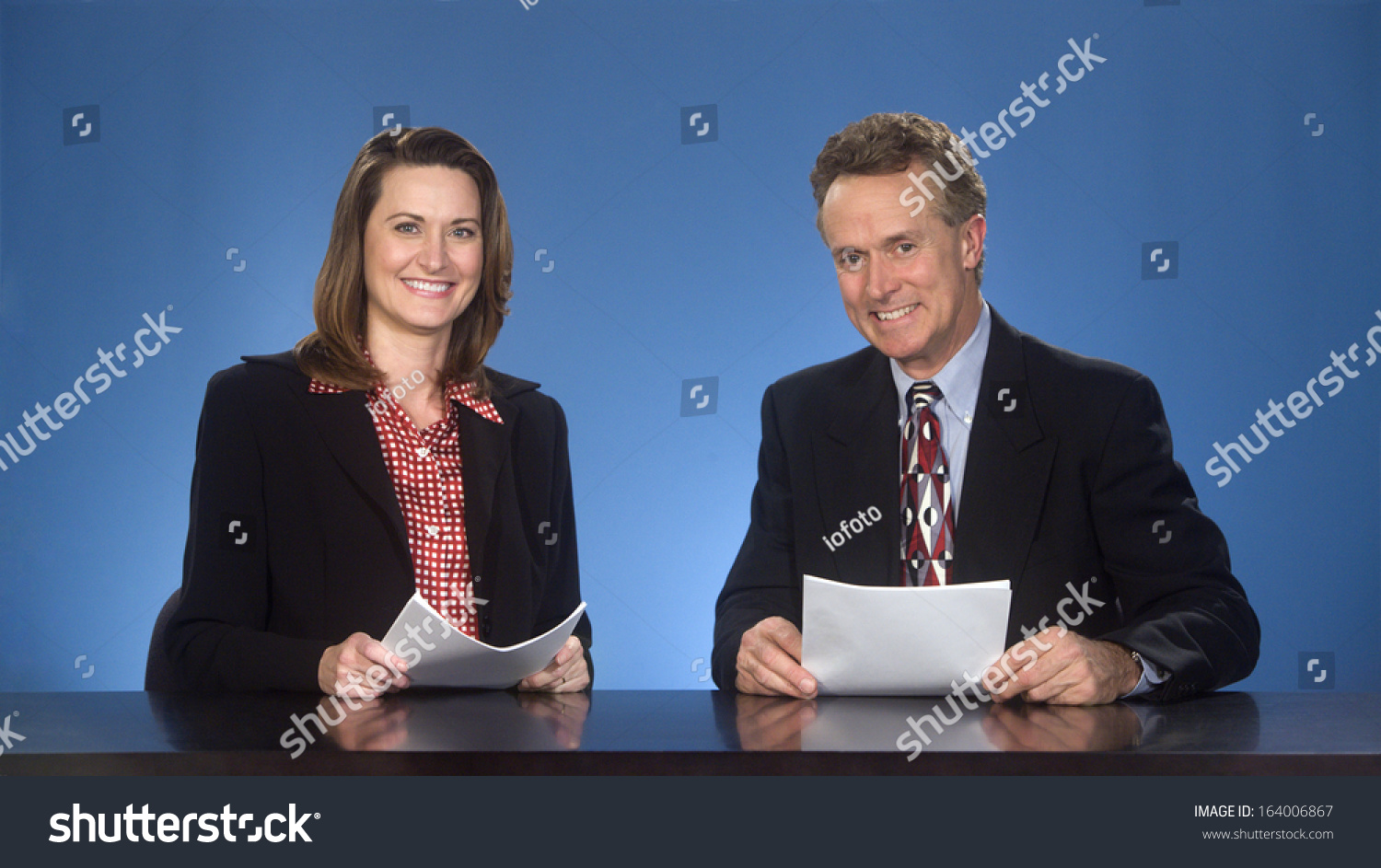 Male and female newscasters sitting at desk smiling at viewer. #164006867