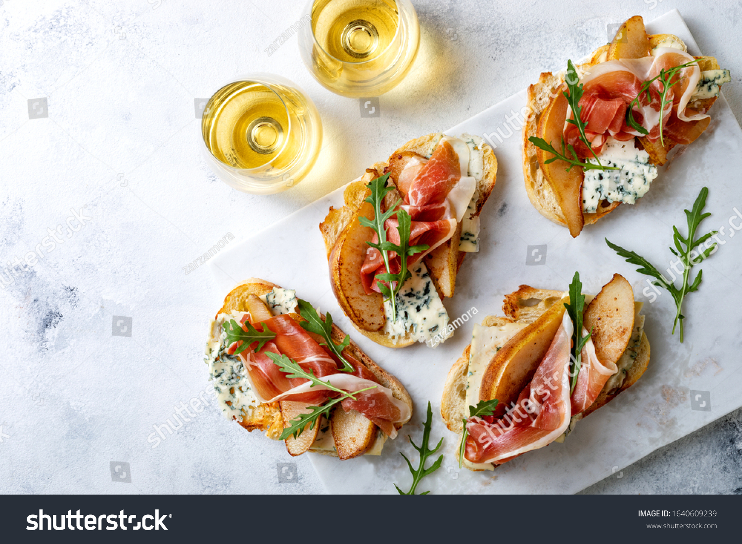 Appetizer crostini, tapas, open faced sandwiches with pear, prosciutto, arugula and blue cheese on white marble board. Delicious snack, appetizers #1640609239