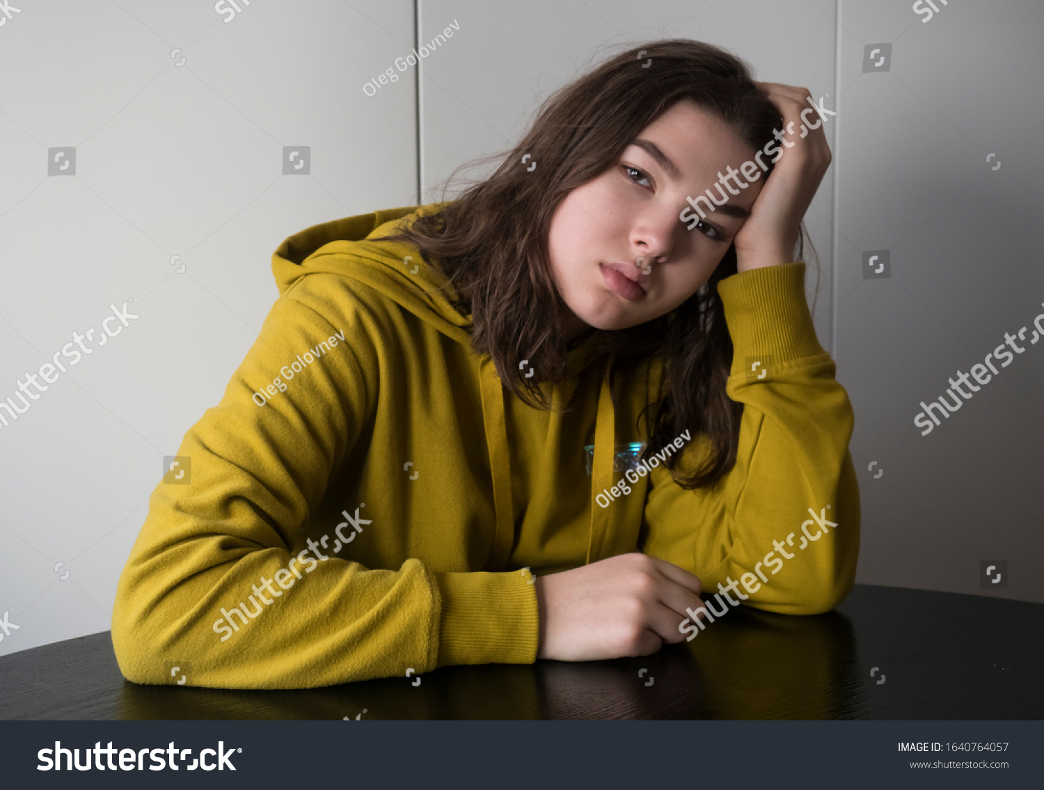 Sad unhappy tired teenager girl sitting at table in room #1640764057