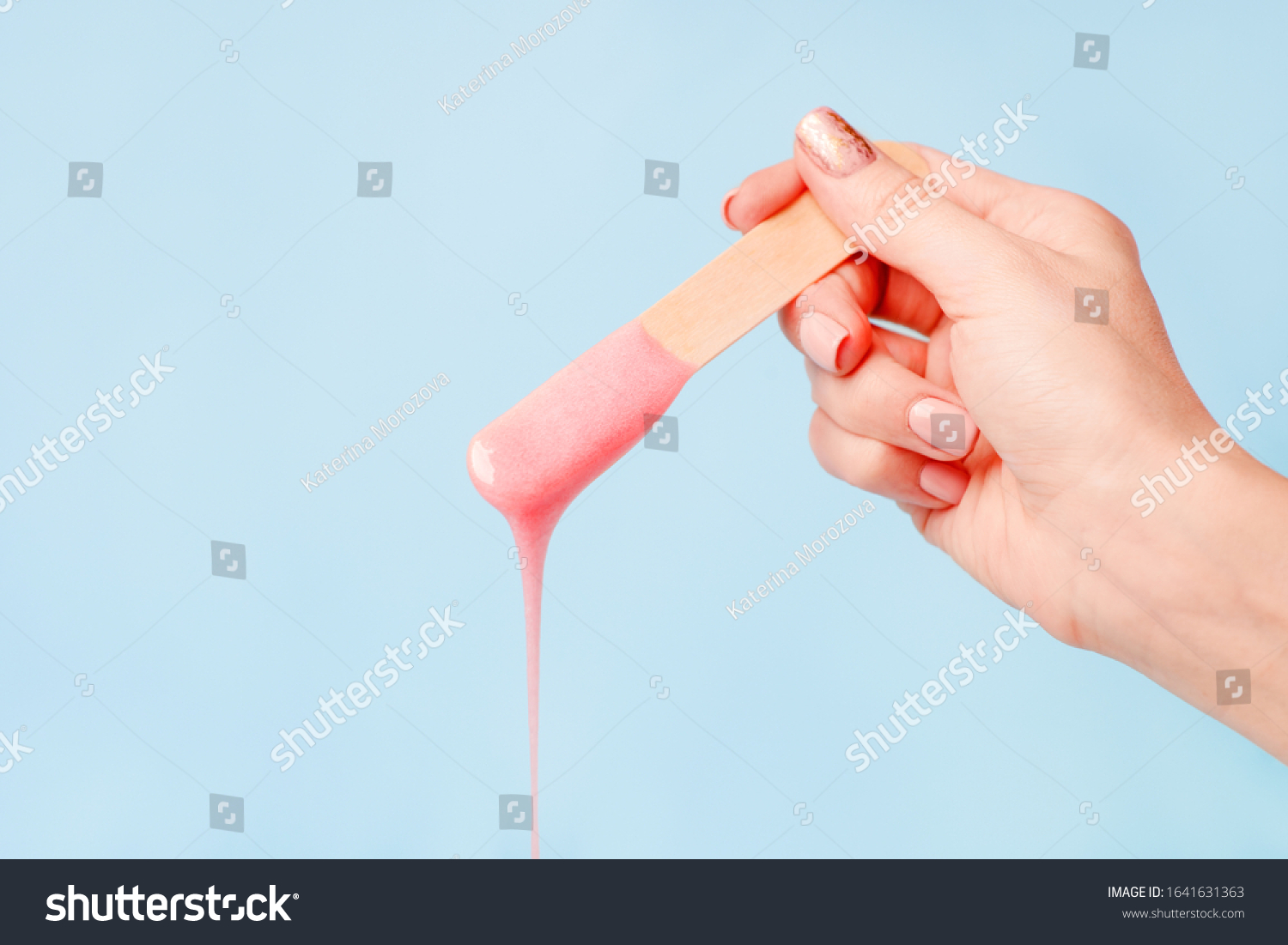 liquid pink pearl wax or sugar paste for depilation drains from the stick on blue background. The concept of depilation, waxing, sugaring smooth skin without hair, banner, copy space #1641631363