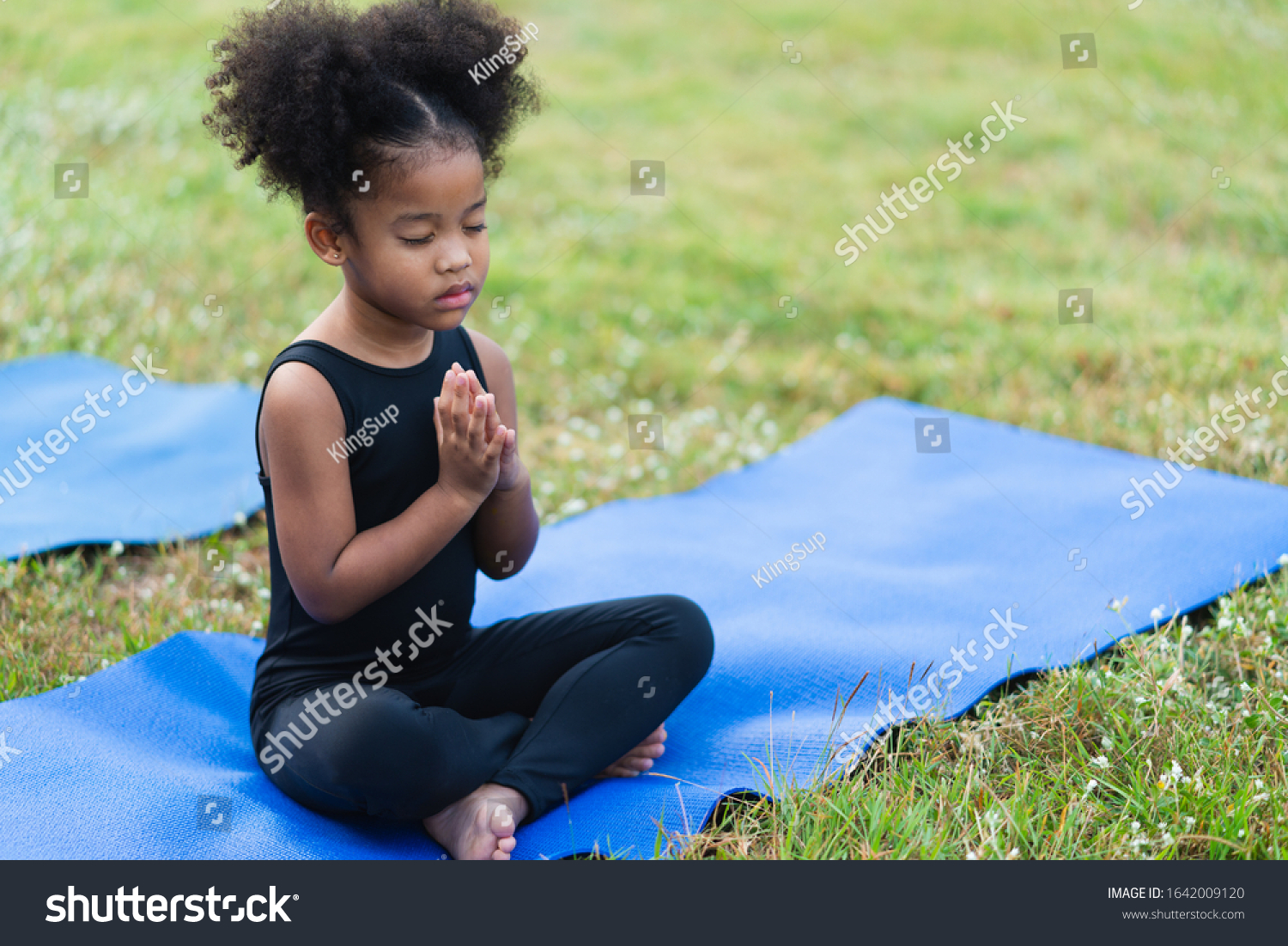 African american little girl sitting on the roll mat practicing meditate yoga in the park outdoor #1642009120