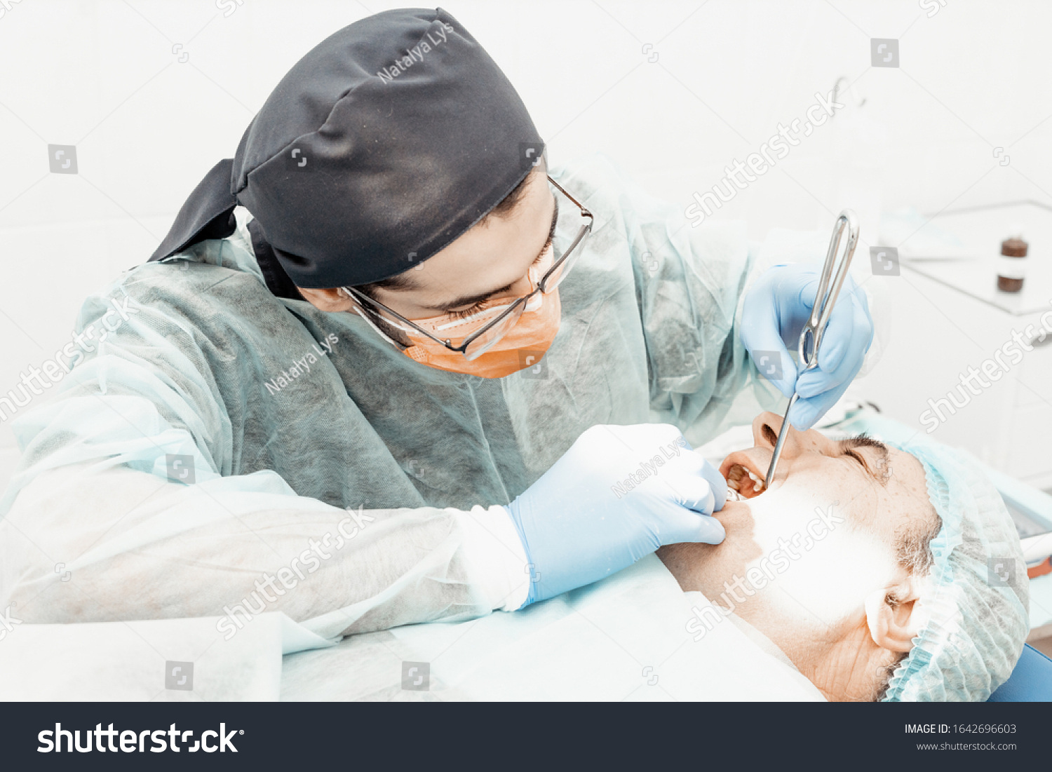 Patient and dentist during implant placement operation. Real operation. Tooth extraction, implants. Professional uniform and equipment of a dentist. Healthcare Equipping a doctor’s workplace.  #1642696603