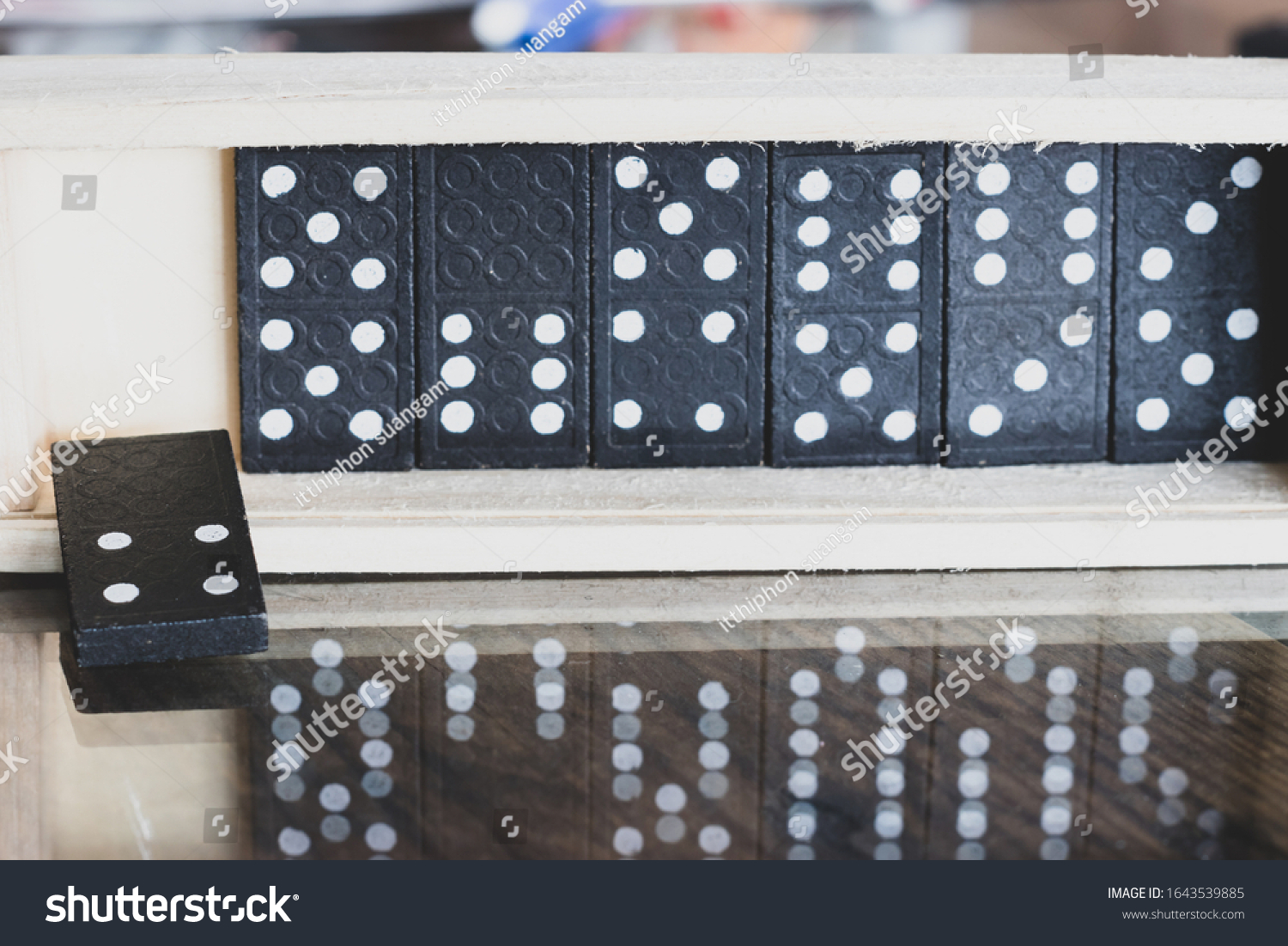 The black Domino Game, made of wood, is placed on a glass-covered wooden table on top. #1643539885