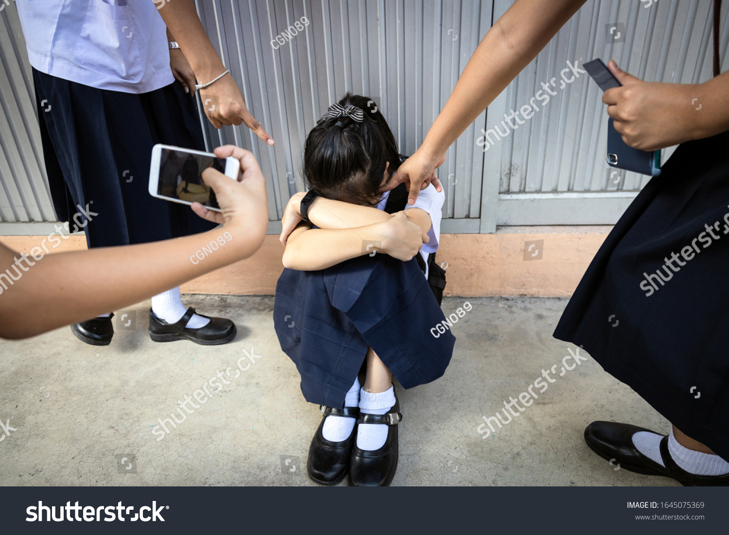 Problems of bullying at school,sad stressed asian girl student crying sitting on the floor,group of hands pointing finger to scared schoolgirl, bullying victim being video recorded on a mobile phone #1645075369