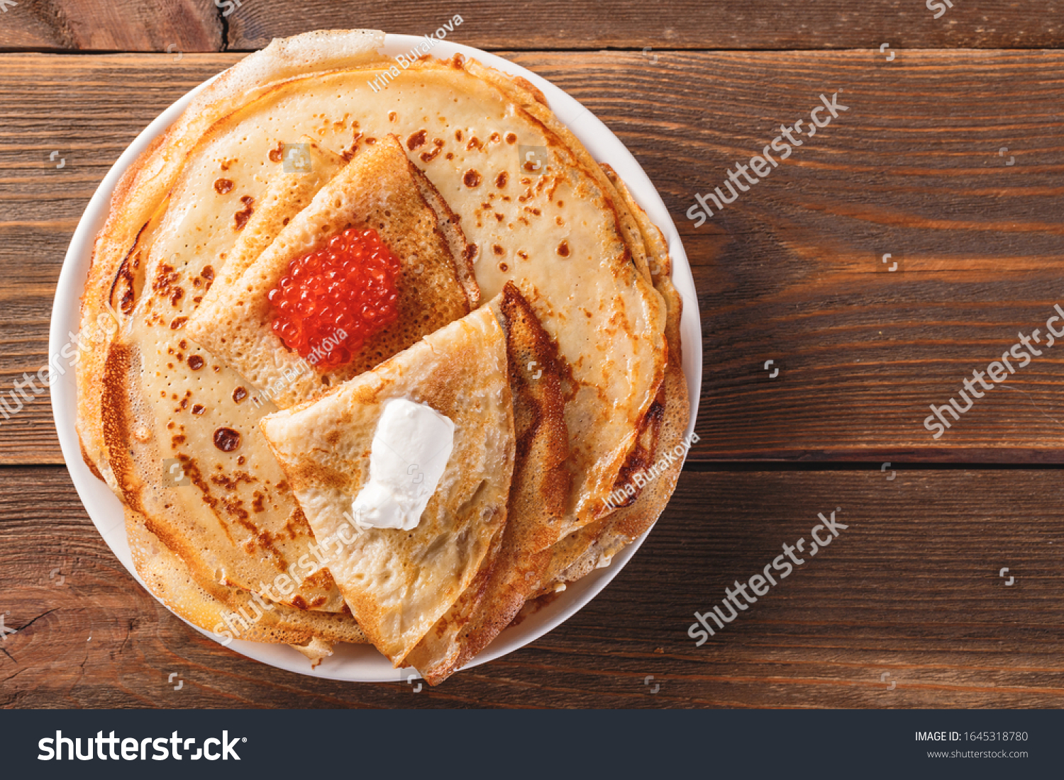 Traditional Russian Crepes Blini stacked in a plate with red caviar, fresh sour creamon dark wooden table. Maslenitsa Russian festival meal. Russian food, russian kitchen. Top view. Space for text #1645318780