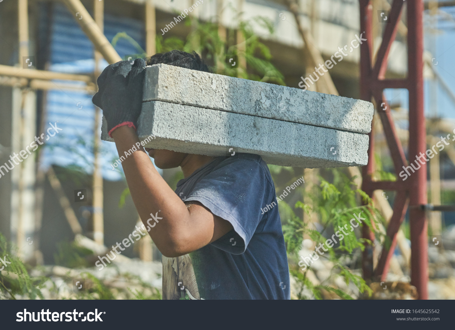 A man on a building construction site carries concrete blocks on his shoulder.   #1645625542