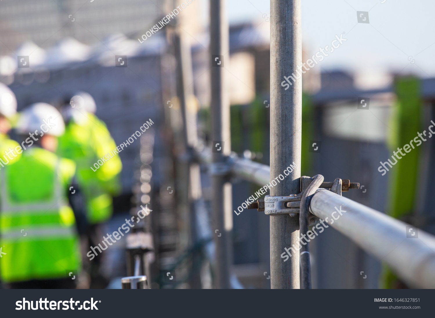 Architect on site Silhouette Construction workers on a scaffold. Extensive scaffolding providing platforms for work in progress. Men walking on roof surrounded by scaffold - Focus on scaffolding frame #1646327851