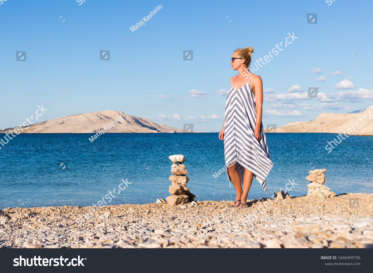 Happy carefree woman wearing beautiful striped summer dress enjoying late afternoon walk on white pabbled beach on Pag island, Croatia. #1646409736