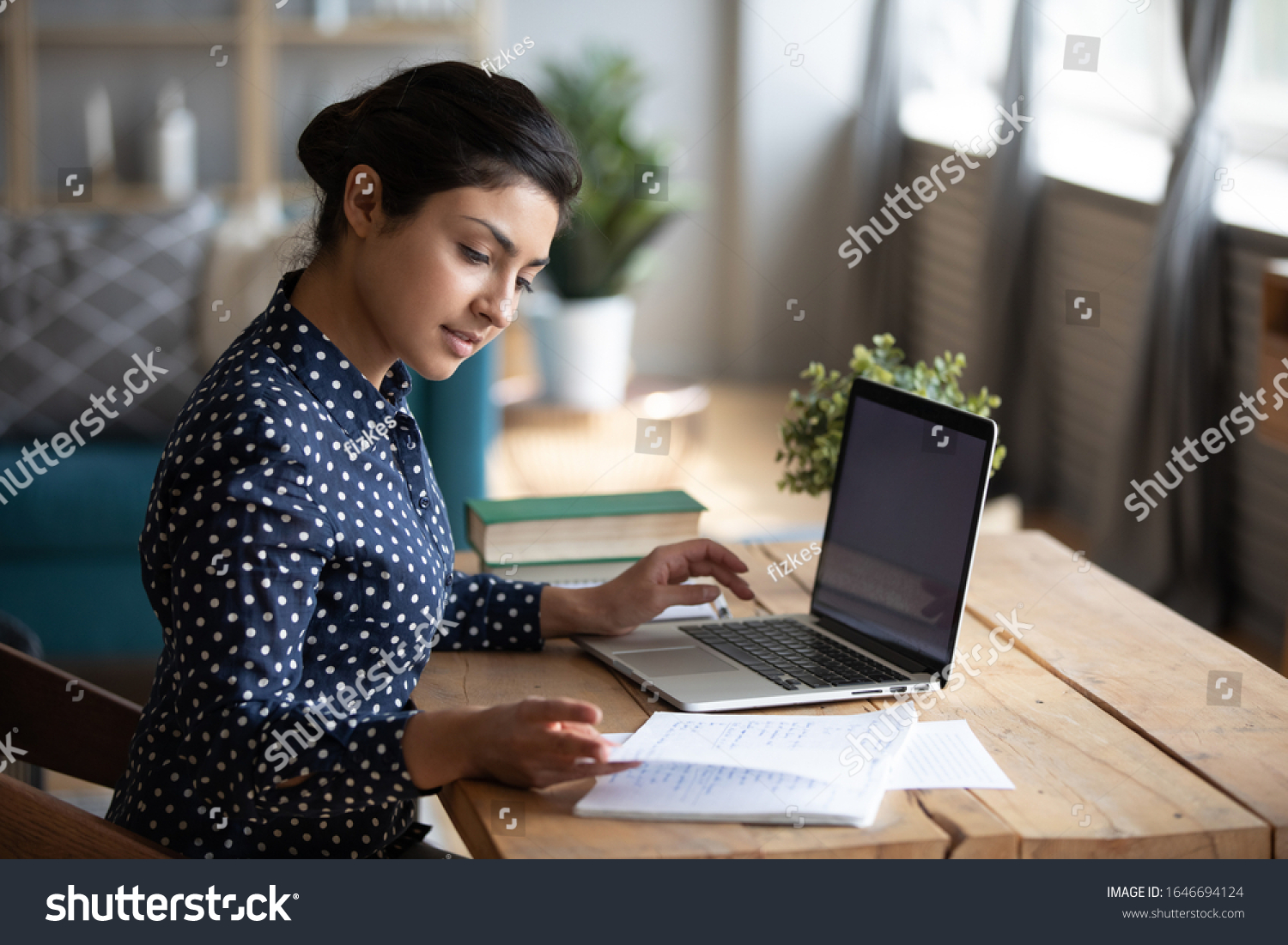Millennial Indian girl sit at desk in living room study on laptop making notes, concentrated young woman work on computer write in notebook, take online course or training at home, education concept #1646694124