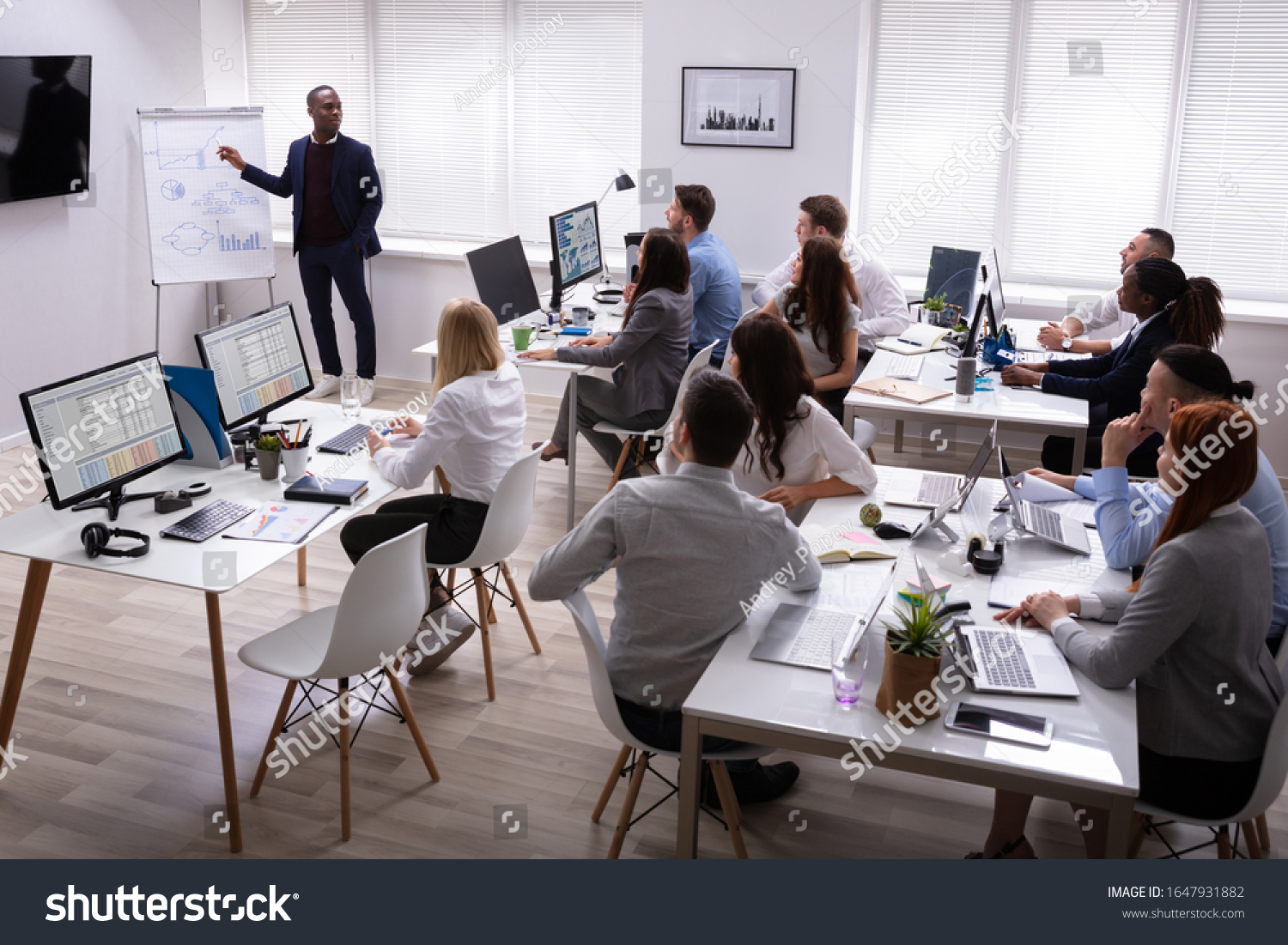 African Businessman Giving Presentation To His Colleagues Sitting On Table With Computers In Office #1647931882