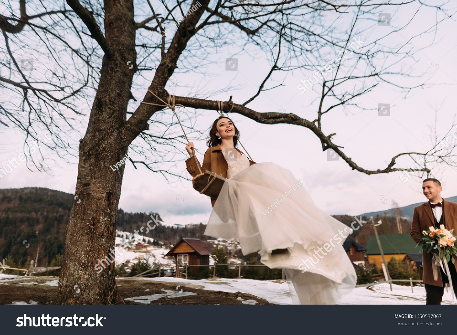 a cheerful and cheerful bride sways on a swing, laughs merrily and enjoys life. Stylish couple in love. #1650537067