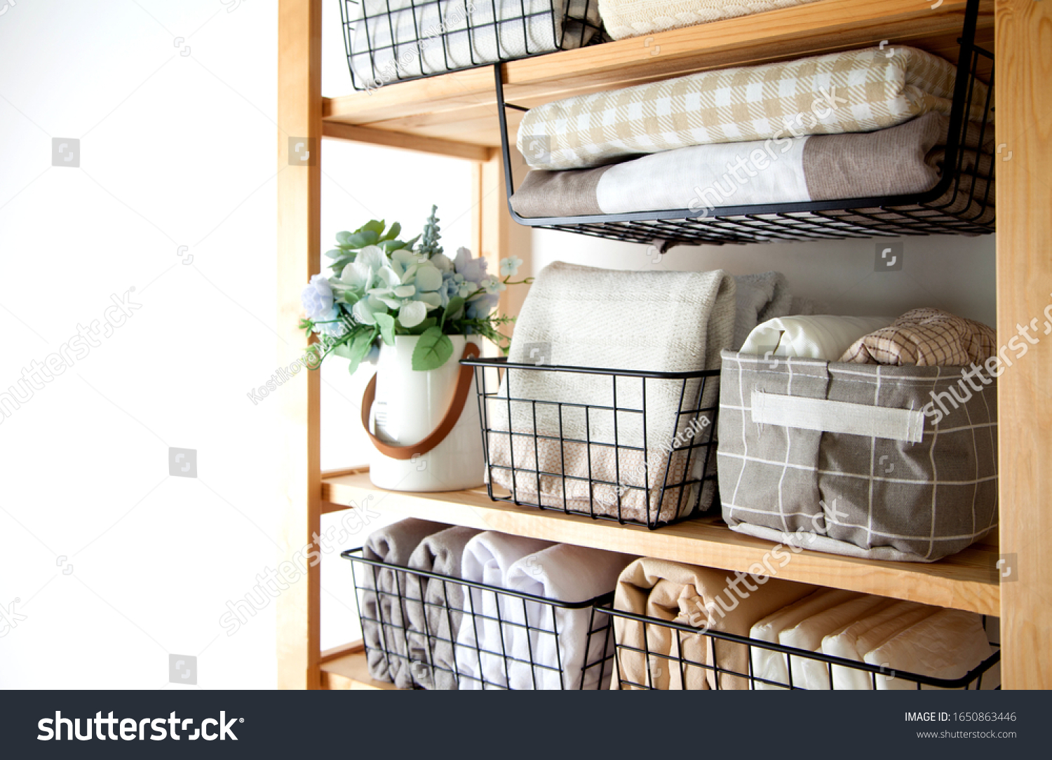 Spring cleaning of closet. Vertical tidying up storage. Neatly folded bed sheets in the metal black baskets for wardrobe. Nordic style. #1650863446