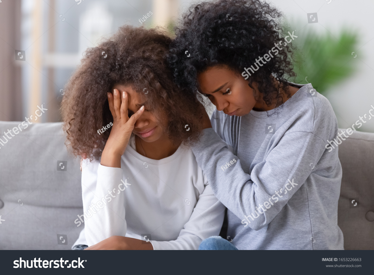 Upset african american mom sister hugging sad child teen girl consoling supporting or asking for forgiveness after fight, black mother hugging comforting depressed teenage daughter sitting on sofa #1653226663
