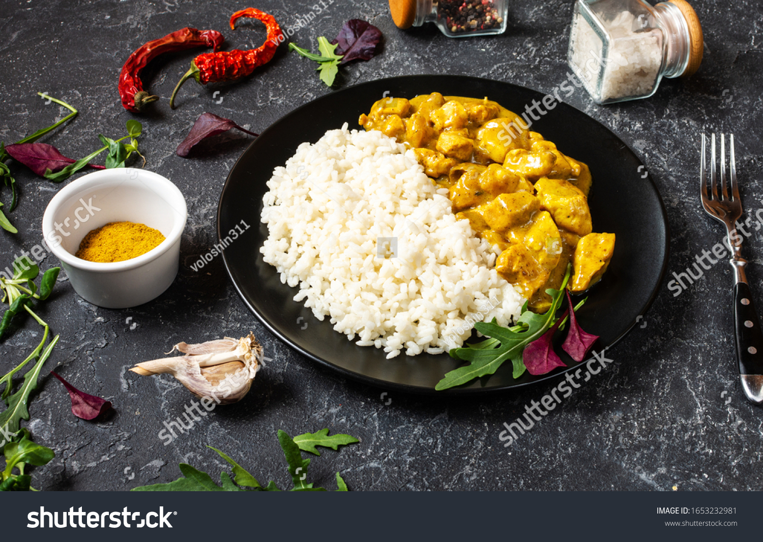 Rice with chicken in curry sauce on plate on black stone background #1653232981