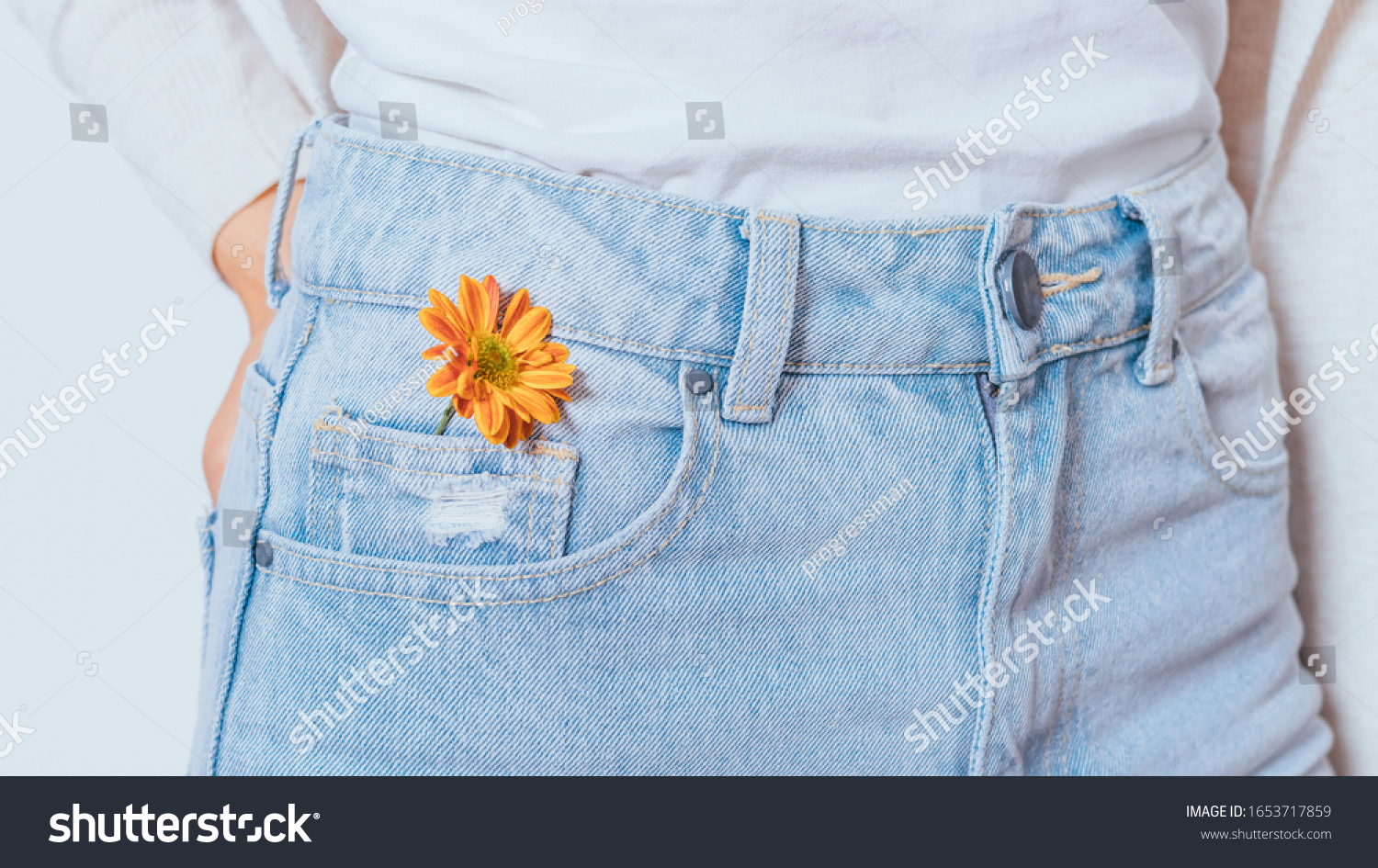 Bright orange flower in pocket blue jeans of young slender woman standing on white background, close-up. #1653717859
